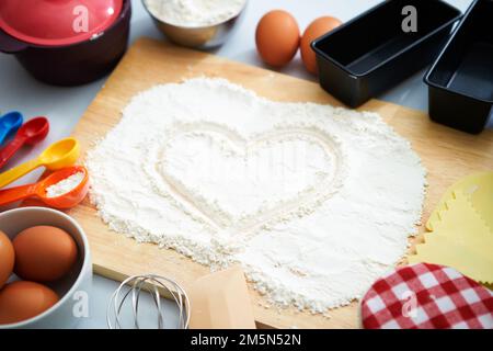 Verschiedene Küchenutensilien und ein auf Mehl gezeichnetes Herz Stockfoto