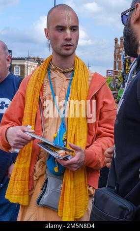 Hare Krishna, ein Liebhaber in safranfarbenen Bademantel, verkauft Bücher und spricht mit Menschen auf den Straßen von Camden Town, London, England Stockfoto