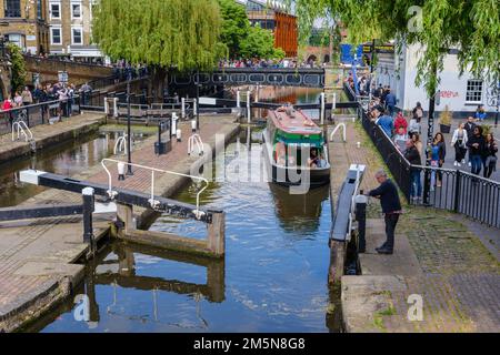 Ein Mann öffnet das Schleusentor, während ein Schmalboot in der Schleusenkammer am Camden Lock am Regent's Canal, einem beliebten Touristenziel, London, wartet Stockfoto