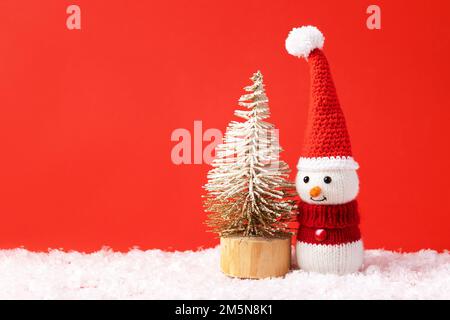 Weihnachtsmärchen-Komposition eines gestrickten Schneemanns mit Weihnachtsmann-Hut und -Pullover. Kleiner Weihnachtsbaum. Stockfoto