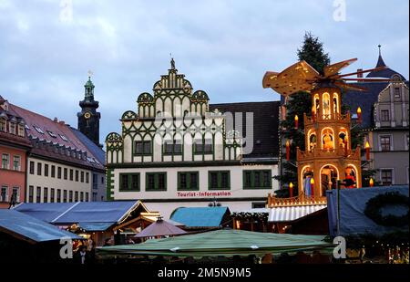 Weimar, Deutschland. 22. Dezember 2022. Blick über die Verkaufsstände des Weimarer Weihnachtsmarkts in Richtung der Stadtburg. In der Mitte des Platzes vor dem Rathaus dreht sich eine Weihnachtspyramide neben dem Weihnachtsbaum, der mit einer Lichterkette dekoriert ist. Kredit: Soeren Stache/dpa/Alamy Live News Stockfoto