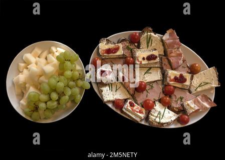 Teller mit Sandwiches und einem Teller mit Melonenstücken und Trauben auf schwarzem Hintergrund, Mecklenbuirg-Vorpommern, Deutschland Stockfoto