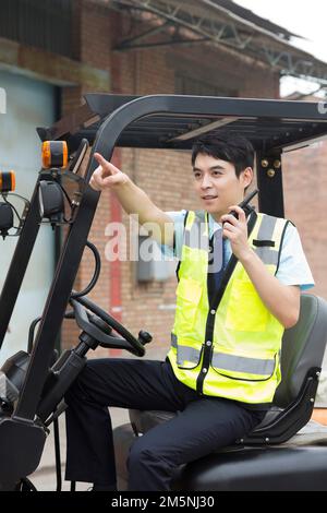 Logistikarbeiter, die Gabelstapler fahren, Handsprechanlage Stockfoto