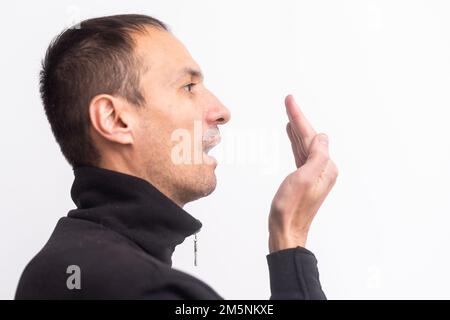 Der Mensch überprüft seinen Atem mit der Hand. Das Konzept der Mundgeruch. Stockfoto