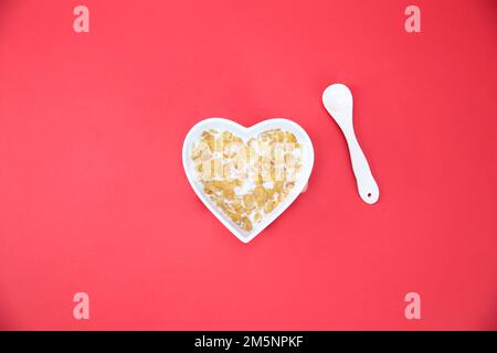 Cornflakes in herzförmiger Schüssel auf rotem Hintergrund Stockfoto