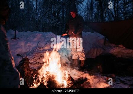 USA Christopher Gracia, aus Miami stammend, und ein Schütze mit 3. Bataillon, 6. Marineregiment, 2D. Marine Division, II Marine Expeditionary Force, steht vor der Übung Cold Response 2022 vor einem Feuer, Setermoen, Norwegen, 26. Februar 2022. Übung Cold Response '22 ist eine alle zwei Jahre stattfindende norwegische nationale Bereitschafts- und Verteidigungsübung, die in ganz Norwegen stattfindet, unter Beteiligung jedes seiner Militärdienste sowie von 26 weiteren alliierten Nationen und regionalen Partnern der Nordatlantikvertrags-Organisation (NATO). Stockfoto