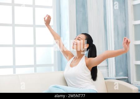 Die junge Frau, die auf dem Sofa sitzt Stockfoto