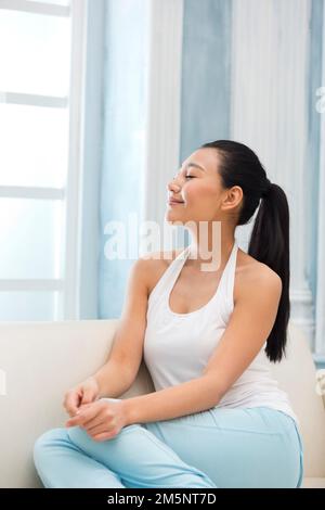 Die junge Frau, die auf dem Sofa sitzt Stockfoto