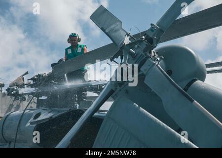 220226-N-GF955-1070 KARIBISCHES MEER - (26. Februar 2022) -- Aviation Machinist Mate 3. Klasse Isaiah Stewart zugewiesen zum "Shadow Det" des Hubschraubers Sea Combat Squadron (HSC) 28, Einheit 7 26, wäscht einen MH-60s Sea Hawk Hubschrauber an Bord des Freiheitsvarianten Küstenschiff USS Billings (LCS, 2022. Februar 15). Billings wird in das US-Flottengebiet 4. entsandt, um die Mission der Joint Interagency Task Force South zu unterstützen, zu der auch Missionen zur Bekämpfung des illegalen Drogenhandels in der Karibik und im östlichen Pazifik gehören. Stockfoto