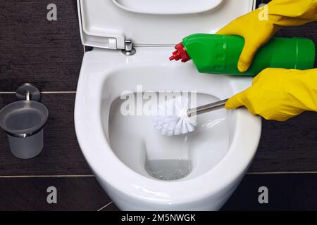 Person in gelben Gummihandschuhen reinigt die Toilettenschüssel mit einer Bürste und einem Desinfektionsmittel Stockfoto