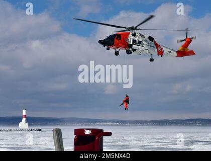 Petty Officer 3. Class James Lowen, ein Rettungsschwimmer der Air Station Traverse City, schweift einen simulierten Überlebenden direkt aus einem Loch im Eis während einer Masseneisrettungsübung am 26. Februar 2022 in der städtischen Marina von Petoskey. Die Übung, bei der der Absturz eines Pendlerflugzeugs auf dem gefrorenen Lake Michigan simuliert wurde, brachte mehr als 100 Ersthelfer und Mitglieder der Küstenwache aus dem gesamten Norden von Michigan zusammen. Foto der US-Küstenwache vom Chief Petty Officer John Masson. Stockfoto
