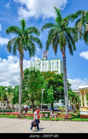 Kubaner gehen im Parque Leoncio Vidal im Stadtzentrum spazieren. Das Hotel Santa Clara Libre befindet sich im Hintergrund Stockfoto