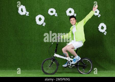Der graskreative junge Mann, der Fahrrad fährt Stockfoto