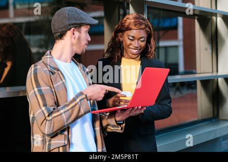 Geschäftskollegen, die ein Notebook verwenden, während sie im Freien über ihre Arbeit sprechen. Stockfoto
