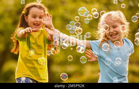 Zwei fröhliche niedliche Mädchen spielen draußen mit riesigen Seifenblasen Stockfoto