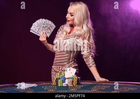 Eine blonde Frau mit perfekter Frisur und leuchtendem Make-up posiert mit Spielkarten in der Hand. Kasino, Poker. Stockfoto