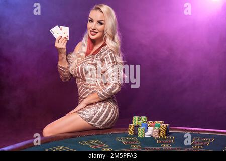 Eine blonde Frau mit perfekter Frisur und leuchtendem Make-up posiert mit Spielkarten in der Hand. Kasino, Poker. Stockfoto