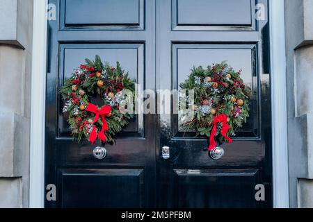 Traditionelle grüne, rote und weiße Weihnachtskränze auf einer schwarzen Doppeltür eines englischen Hauses in London, Großbritannien. Stockfoto