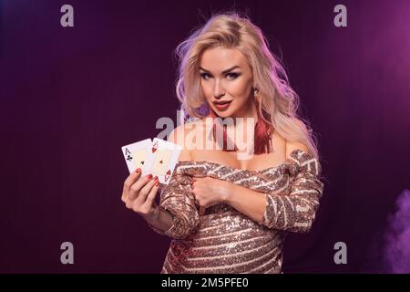 Eine blonde Frau mit perfekter Frisur und leuchtendem Make-up posiert mit Spielkarten in der Hand. Kasino, Poker. Stockfoto