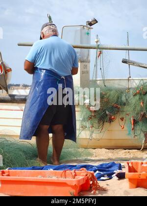 Viele Fische, die mit einem Fischer auf einem Boot in einem Fischernetz gefangen wurden Stockfoto