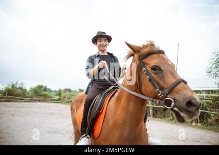 Junger Mann mit Cowboyhut, der beim Reiten Zügel in der Hand hält Stockfoto