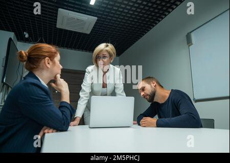 Blonde, rothaarige Frau und bärtiger Mann in Anzügen im Büro. Geschäftsleute verhandeln im Konferenzraum. Stockfoto