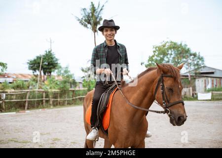 ein asiatischer Mann mit Cowboyhut, reitet auf Pferden und hält Zügel Stockfoto