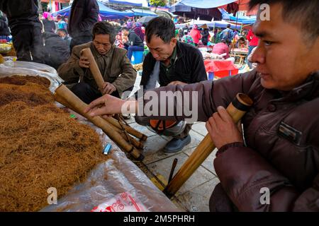 BAC Ha, Vietnam - 18. Dezember 2022: Männer, die auf dem Wochenmarkt von Bac Ha in Vietnam Tabak rauchen. Stockfoto