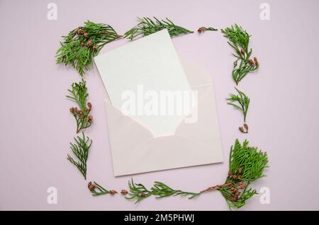 Minimalistisches Kartenmodell mit Rahmen aus Thuja-Zweigen. Handgefertigter Umschlag, Karte, flach liegend, Draufsicht. Entwurf der Einladungsvorlage. Arborvitae. Stockfoto