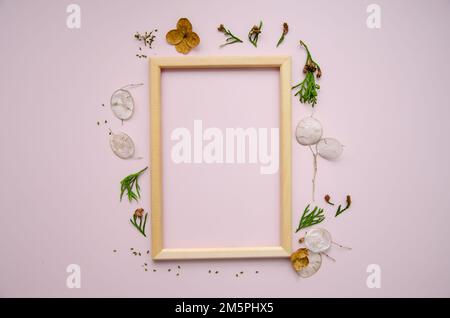 Leerer Holzrahmen auf pinkfarbenem Hintergrund mit getrockneten Lunaria- und Gartenblumen und Thuja-Ästen. Mockup-Posterrahmen Nahaufnahme in neutraler Farbe, minim Stockfoto