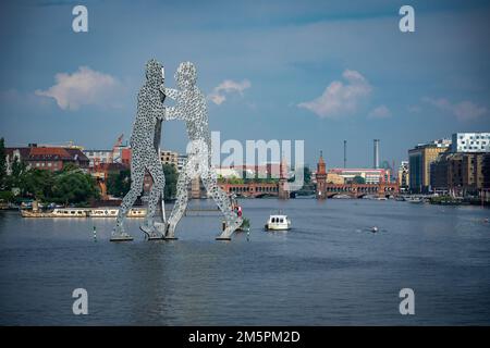 Berlin, Deutschland - Juni 25 2022: Die Skulptur des Riesenmolekül-Mannes in Ostberlin erhebt sich von der Spree mit der Oberbaumbrücke in der Ferne Stockfoto