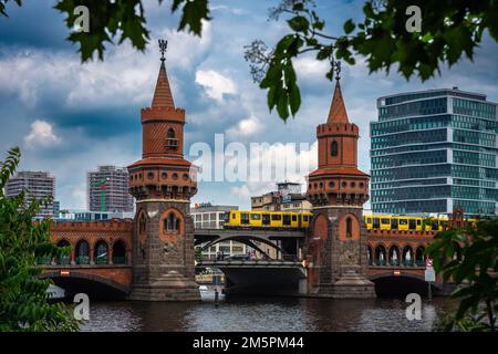 Berlin, Deutschland - Juni 25 2022: Berlins Symbol: Die Oberbaumbrücke, eingerahmt von Ästen, während eine hellgelbe Straßenbahn durchfährt Stockfoto