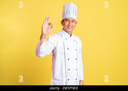 asiatischer männlicher Koch, der mit einer guten Handbewegung lächelt Stockfoto