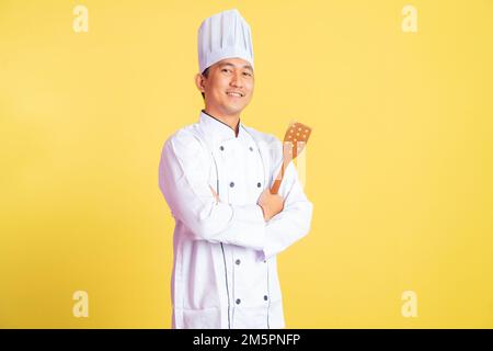 Lächelnder asiatischer Koch, der einen Teigschaber mit gekreuzten Händen hält Stockfoto