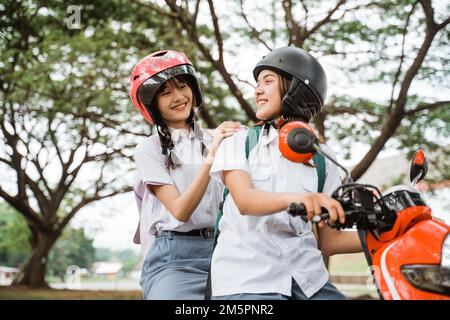 Zwei Schülerinnen, die Helme tragen und sich beim Motorradfahren unterhalten Stockfoto