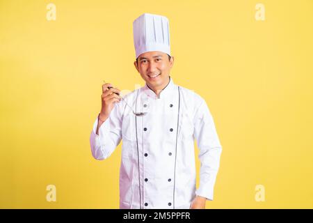 Lächelnder Koch mit einer Kelle, der Essen schmeckt Stockfoto