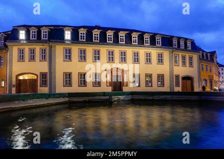 Weimar, Deutschland. 22. Dezember 2022. Das Goethe-Haus im Frauenplan kann am Abend hinter der Wasseroberfläche des Brunnens gesehen werden. Johann Wolfgang von Goethe lebte bis zu seinem Tod fast 50 Jahre im Goethehaus, das 1709 erbaut wurde. Das Gebäude der Klassik Stiftung Weimar, das zum UNESCO-Weltkulturerbe gehört, ist Teil des Ensembles des Goethe-Nationalmuseums und soll ab 2026 renoviert werden. Kredit: Soeren Stache/dpa/Alamy Live News Stockfoto