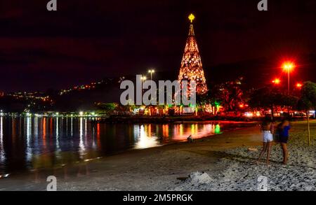 Zwei Frauen stehen nachts in San Francisco Beach im Sand. Die Lichter der Stadt und der Weihnachtsbaum in der Ferne spiegeln sich im Wasser wider. Lange Belichtung Stockfoto