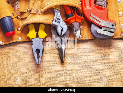 Spitzmaulschlüssel Zange Stahlschneider Schraubendreher im Werkzeuggürtel auf Holzplatte Stockfoto