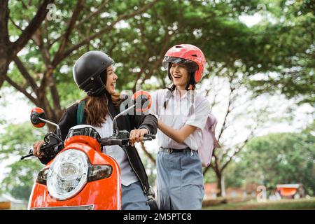 Zwei Freunde, die Helme tragen, scherzen, wenn sie mit dem Motorrad zur Schule fahren Stockfoto