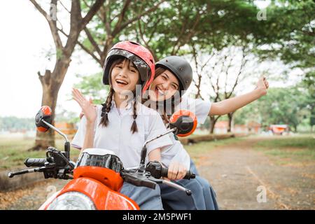 Zwei Schülerinnen mit Helmen winkten, während sie Motorrad fuhren Stockfoto