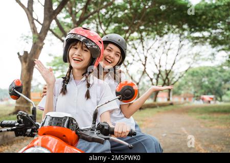 Zwei Schülerinnen lächelten für die Kamera, während sie Motorrad fuhren Stockfoto