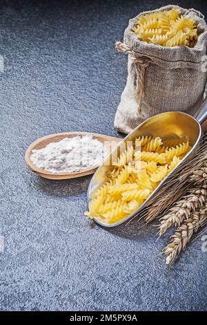 Säcke, ungekochte Nudelküche, Schaufel mit Holzlöffel, Mehl, Weizen, Roggenohren auf schwarzem Hintergrund. Stockfoto