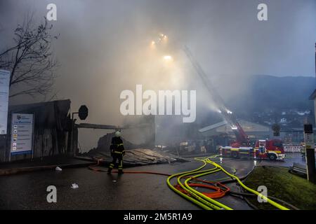 Wehr, Deutschland. 30. Dezember 2022. Der Korb einer Plattenleiter steht in einer Mischung aus Rauch und Dampf, während ein Feuerwehrmann im Vordergrund steht. Ein Brand in mehreren Gebäuden an einem Industriestandort hat Schäden im Wert von mehreren Millionen Euro verursacht. Die Feuerwehren waren mit etwa 160 Einsatzkräften vor Ort. Kredit: Philipp von Ditfurth/dpa/Alamy Live News Stockfoto