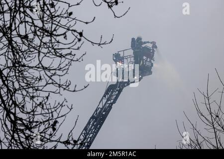 Wehr, Deutschland. 30. Dezember 2022. Ein Feuerwehrmann steht auf einer Drehteller-Leiter und löscht ein Feuer. Ein Brand in mehreren Gebäuden an einem Industriestandort verursachte Schäden im Wert von mehreren Millionen Euro. Die Feuerwehren waren mit etwa 160 Einsatzkräften vor Ort. Kredit: Philipp von Ditfurth/dpa/Alamy Live News Stockfoto