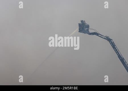 Wehr, Deutschland. 30. Dezember 2022. Ein Feuerwehrmann steht auf einer Drehteller-Leiter und löscht ein Feuer. Ein Brand in mehreren Gebäuden an einem Industriestandort verursachte Schäden im Wert von mehreren Millionen Euro. Die Feuerwehren waren mit etwa 160 Einsatzkräften vor Ort. Kredit: Philipp von Ditfurth/dpa/Alamy Live News Stockfoto