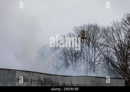 Wehr, Deutschland. 30. Dezember 2022. Ein Feuerwehrmann steht auf einer Drehteller-Leiter und löscht ein Feuer. Ein Brand in mehreren Gebäuden an einem Industriestandort verursachte Schäden im Wert von mehreren Millionen Euro. Die Feuerwehren waren mit etwa 160 Einsatzkräften vor Ort. Kredit: Philipp von Ditfurth/dpa/Alamy Live News Stockfoto