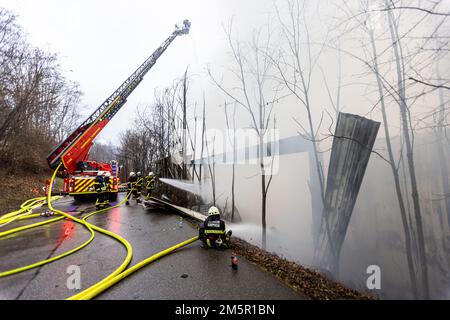 Wehr, Deutschland. 30. Dezember 2022. Feuerwehrleute kühlen eine Industriehalle ab, die seit Mittag in Flammen steht. Ein Brand in mehreren Gebäuden an einem Industriestandort verursachte Schäden im Wert von mehreren Millionen Euro. Die Feuerwehren waren mit etwa 160 Einsatzkräften vor Ort. Kredit: Philipp von Ditfurth/dpa/Alamy Live News Stockfoto