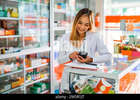 Attraktiver Apotheker in Uniform mit Smartphone während der Arbeit Stockfoto