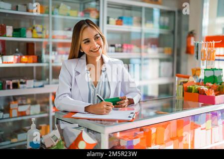 Attraktive Apothekerin, die einen Stift benutzt, um den Arzneimittelnamen auf Papier zu schreiben Stockfoto